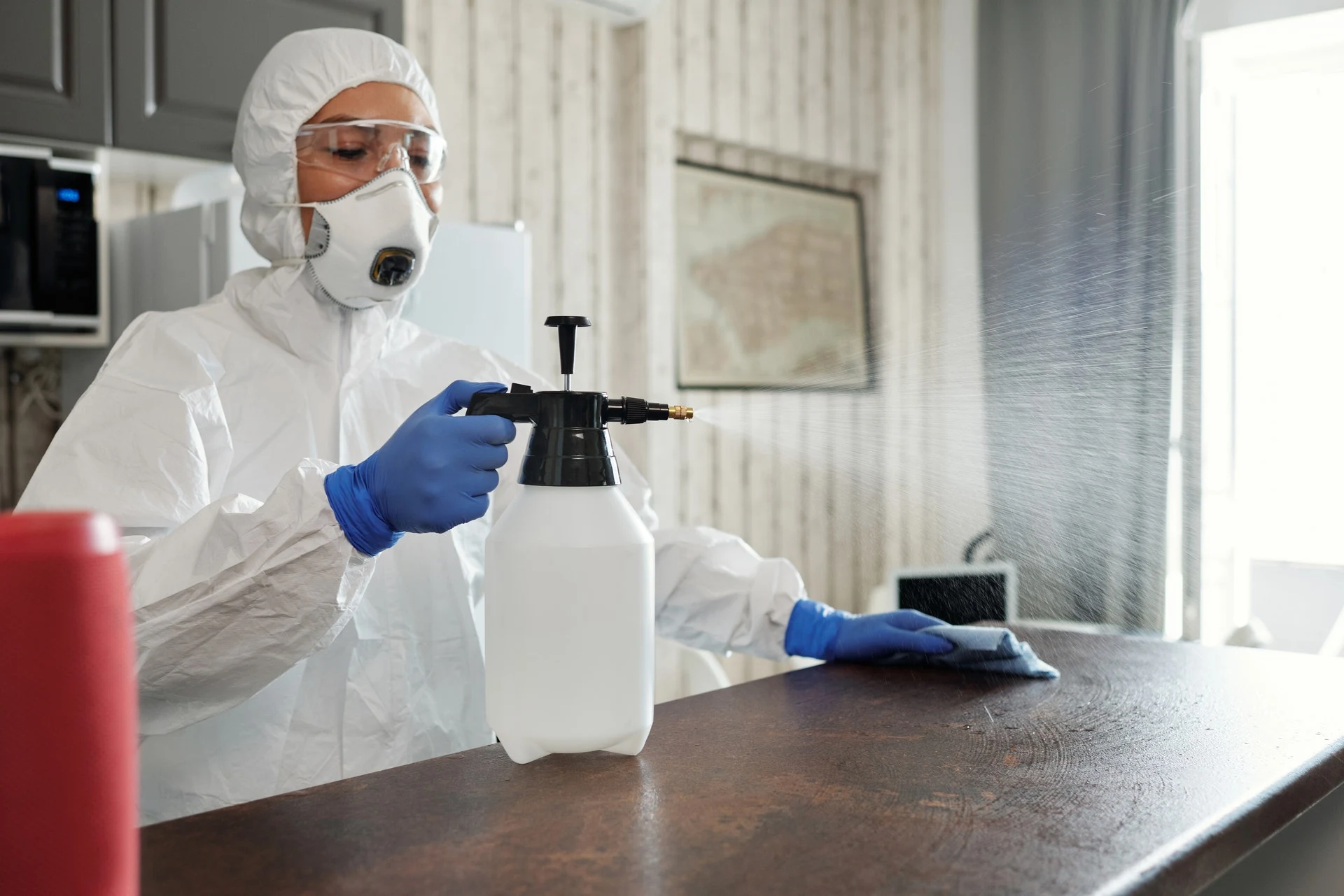 Profesional con equipo de protección sanitizando una superficie interior